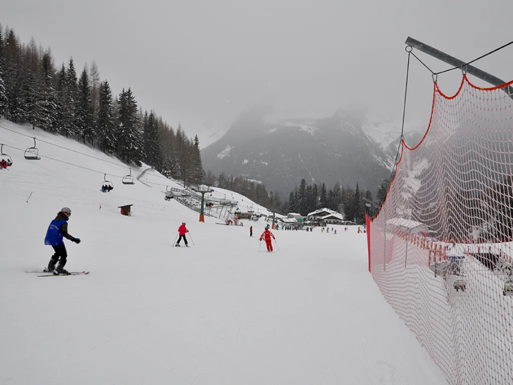 Skifahrende neben einem roten Sicherheitsnetz an der Piste.